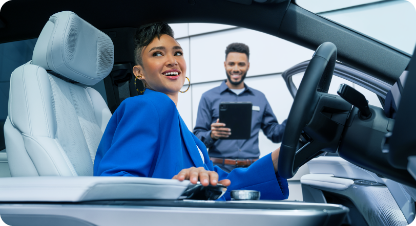 Profile view of woman in sitting in driver seatof Cadillac LYRIQ, man with iPad in background.